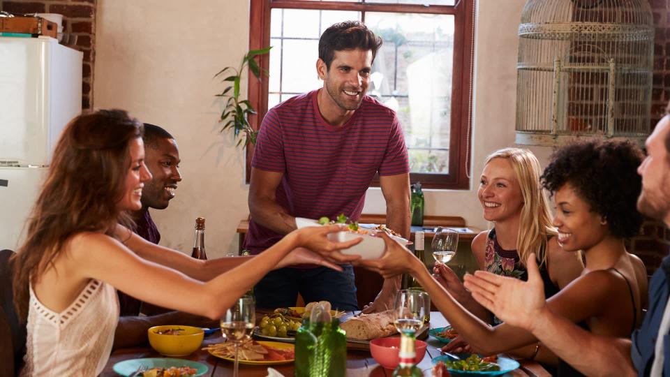 Host and friends pass food round the table at a dinner party