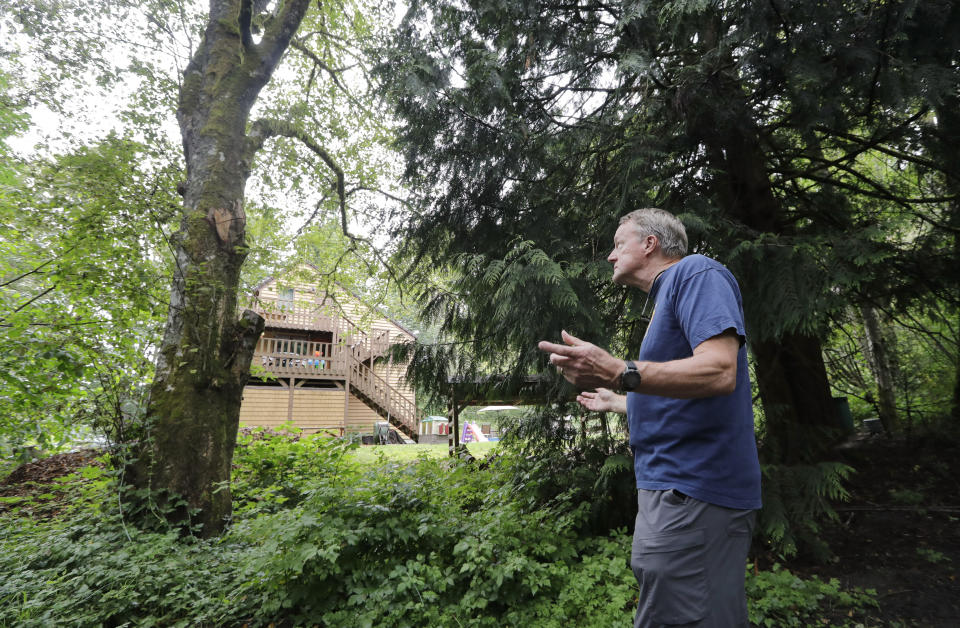 In this photo taken Friday, Aug. 2, 2019, Wayne Elson looks up at a dead tree that he says he needs to cut down, as it could fall and block the road in a fire, as he walks in front of his home in Issaquah, Wash. Elson is the firewise coordinator in the development, his home one of hundreds of houses in his community built into the woods there. (AP Photo/Elaine Thompson)