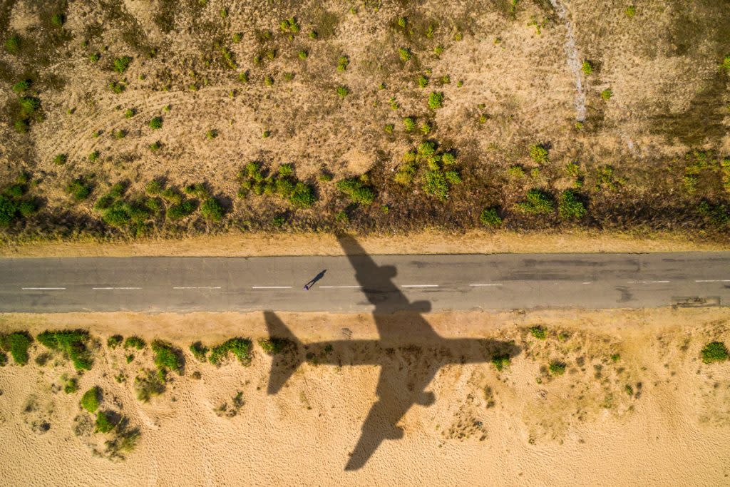 A shadow of a plane sits on a desert terrain with a road in-between the desert. 