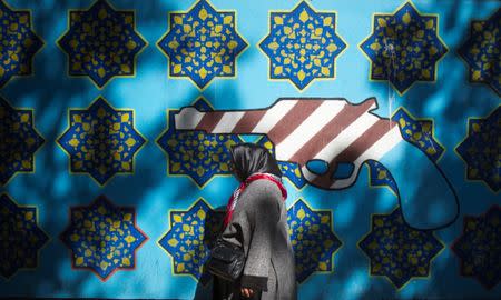 An Iranian woman walks past an anti-U.S. mural on the wall of the former U.S. embassy in Tehran October 12, 2011. REUTERS/Morteza Nikoubazl/Files