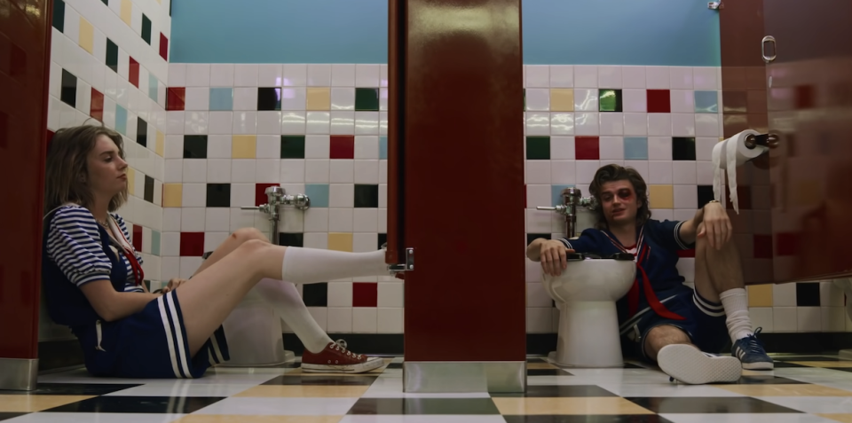 two characters sitting on the floor of the bathroom in different stalls