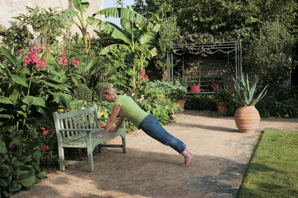 This undated publicity photo released by courtesy Timber Press, shows Bunny Guinness using a garden bench for exercise from the book, “Garden Your Way To Health and Fitness,” by Bunny Guinness and Jacqueline Knox (Design, Bunny Guinness). Gardens can be pathways to better conditioning, when you trade treadmills for trails, exercise mats for lawns and garden benches for weight racks. (AP Photo/Courtesy Timber Press)