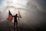 <p>Nyoman Budiartha of Decatur, Ga., holds an American flag and an Indonesian flag as his cools off in a water spray after running the Peachtree Road Race in Atlanta, Ga., Saturday, morning, July 4, 1998. (Photo: John Bazemore/AP) </p>