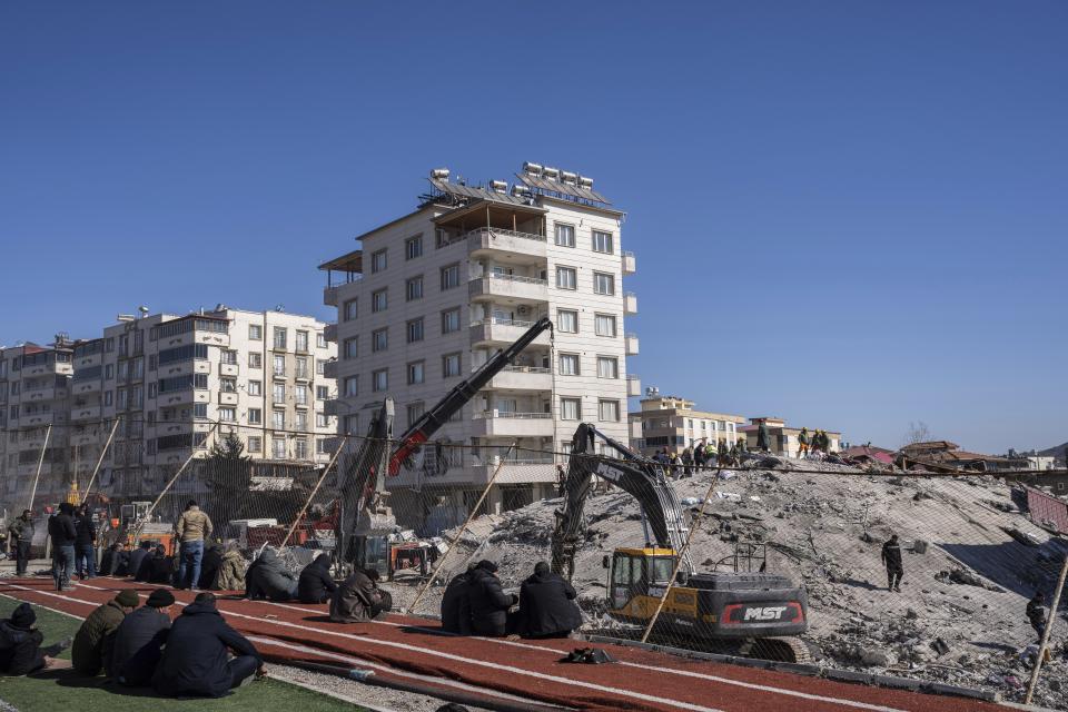 Local residents watch the rescuers and heavy machines searching a destroyed building in Nurdagi, southeastern Turkey, Thursday, Feb. 9, 2023. Thousands who lost their homes in a catastrophic earthquake huddled around campfires and clamored for food and water in the bitter cold, three days after the temblor and series of aftershocks hit Turkey and Syria. (AP Photo/Petros Giannakouris)