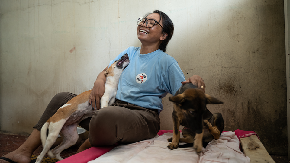 Dog rescuer Rathany Tan smiles as she plays with two young dogs.