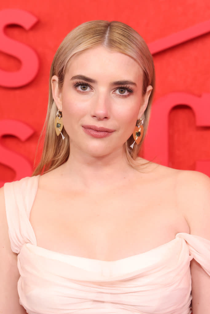 Emma Roberts on a red carpet wearing an elegant off-the-shoulder gown and geometric earrings