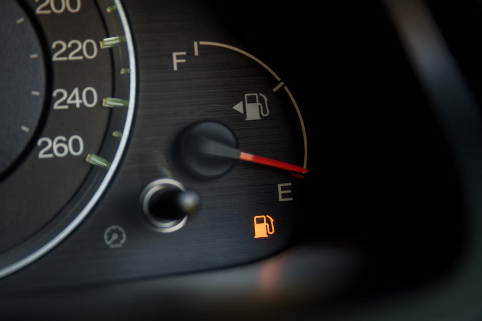 Close-up of a car's fuel gauge showing a near-empty tank with the low fuel warning light illuminated