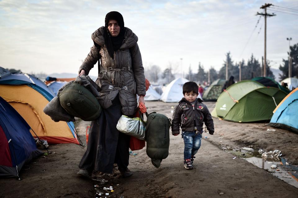 A woman walks with a child as she arrives to a makeshift camp at the Greek-Macedonian border near the Greek village of Idomeni on March 3, 2016. Despite strict new border regulations that allow few to cross, migrants and refugees of&nbsp;all ages continue to make their way to the border.