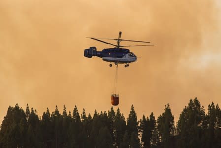 A helicopter carries water to fight a forest fire seen in the village of Valleseco