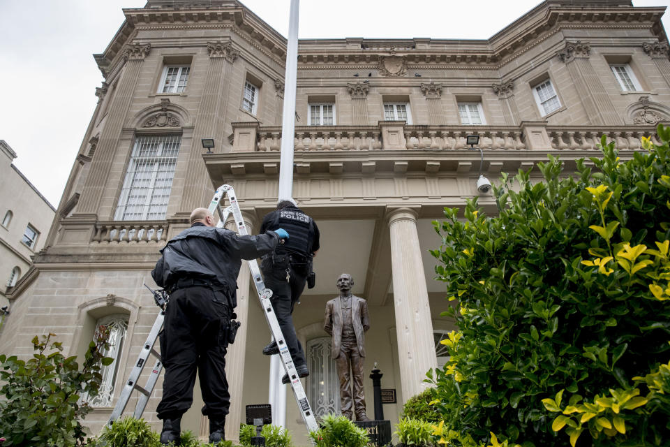 A statue of Cuban national hero Jose Marti is visible behind Secret Service investigators as they look at a bullet hole in the flagpole in front of the Cuban Embassy after police say a person with an assault rifle opened fire, Thursday, April 30, 2020, in Washington. (AP Photo/Andrew Harnik)