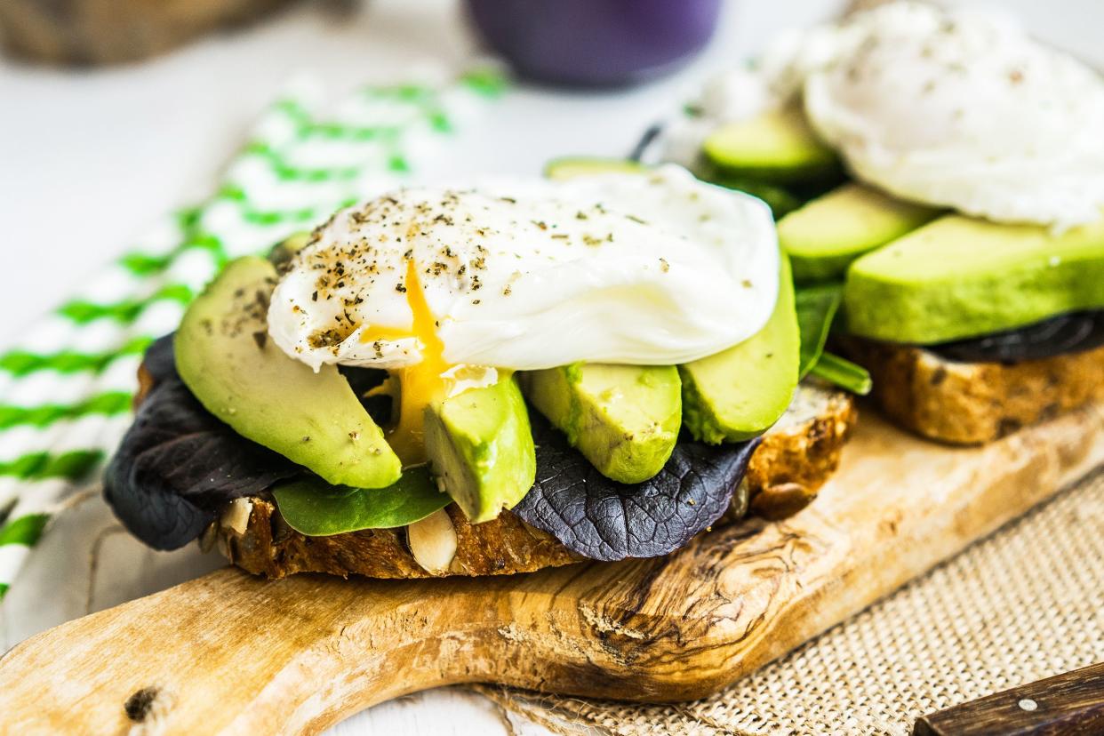 Focus on two pieces of egg and avocado on toast on an olivewood serving board, with a blurred background of napkins