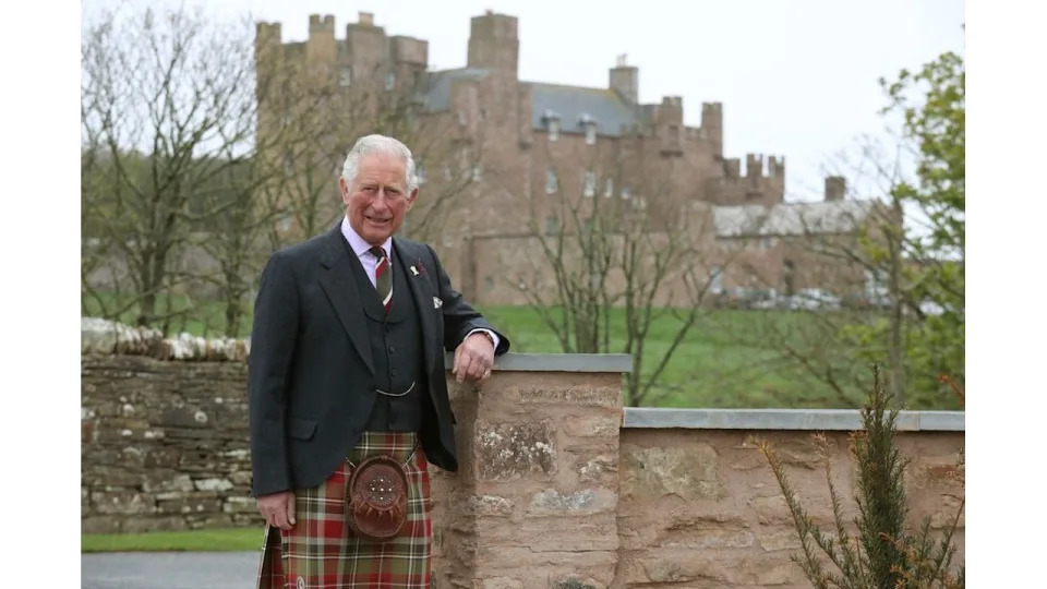 king charles posing in tartan in front of Scottish castle