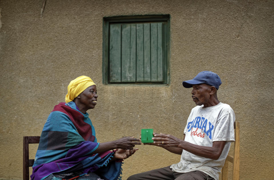 In this photo taken Thursday, April 4, 2019, genocide survivor Laurencia Mukalemera, left, a Tutsi, is offered a cup of water by Tasian Nkundiye, right, a Hutu who murdered her husband and spent eight years in prison for the killing and other crimes, before being interviewed at Nkundiye's home in the reconciliation village of Mbyo, near Nyamata, in Rwanda. Twenty-five years after the genocide the country has six "reconciliation villages" where convicted perpetrators who have been released from prison after publicly apologizing for their crimes live side by side with genocide survivors who have professed forgiveness. (AP Photo/Ben Curtis)