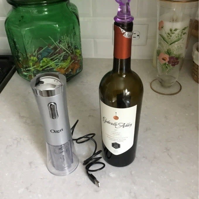 Electric wine opener next to a bottle of wine with a twisted corkscrew attached