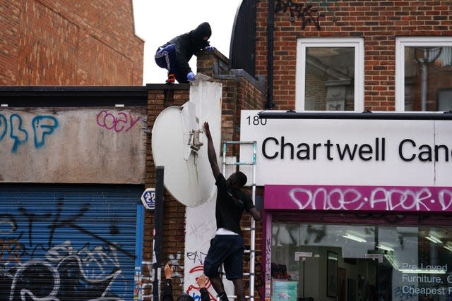 Two people, one on a ladder, taking a satellite dish down from a roof