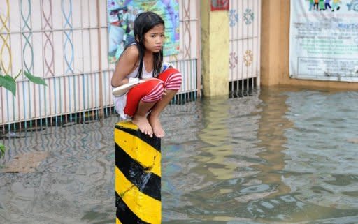 A soaking wet child sits on a post on a flooded street in suburban Manila on August 8, 2012. Twenty people have died from this week's rains in Manila and nearby provinces, according to authorities