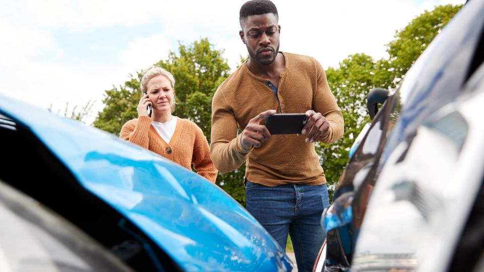 Male Motorist Involved In Car Accident Taking Picture Of Damage For Insurance Claim.