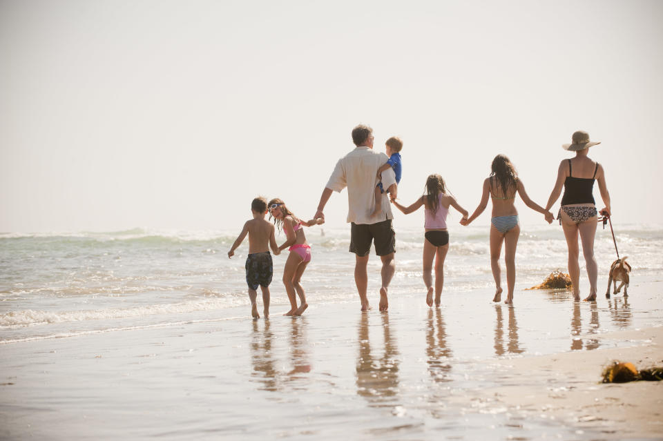 A family of seven holds hands and walks along the beach