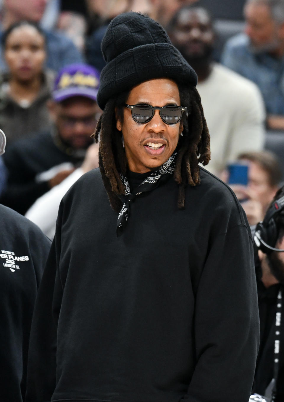 Person in black attire and sunglasses with a knit hat at an event