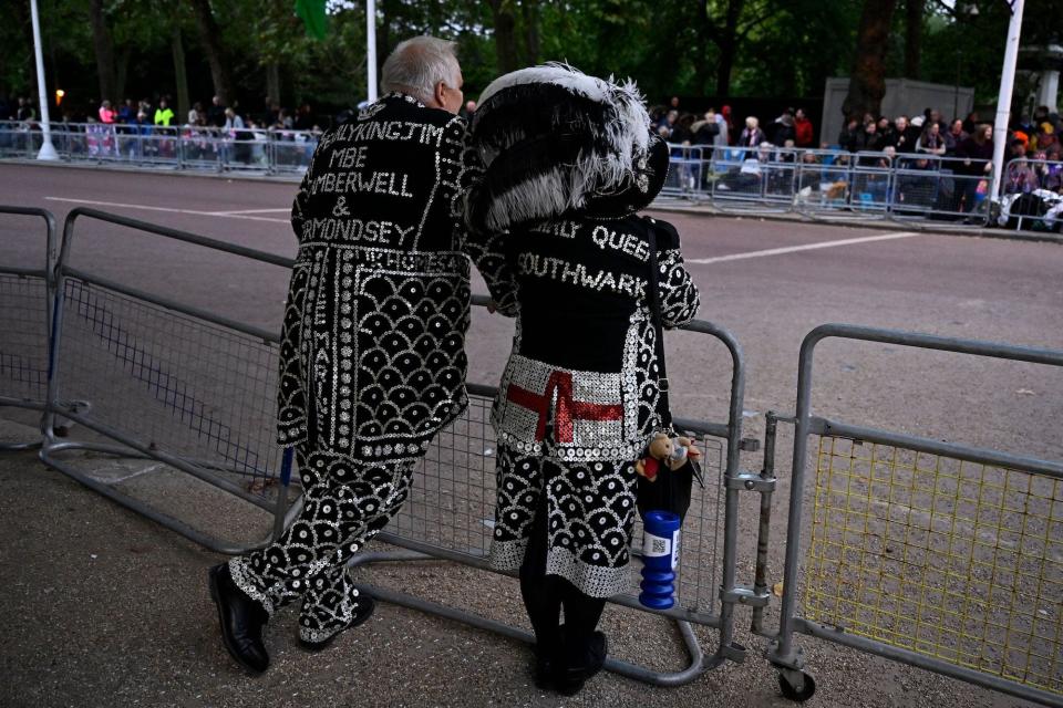 Two people in costume await Queen Elizabeth II's funeral procession.