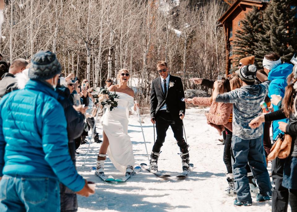 A bride and groom ski into a group of waiting people.