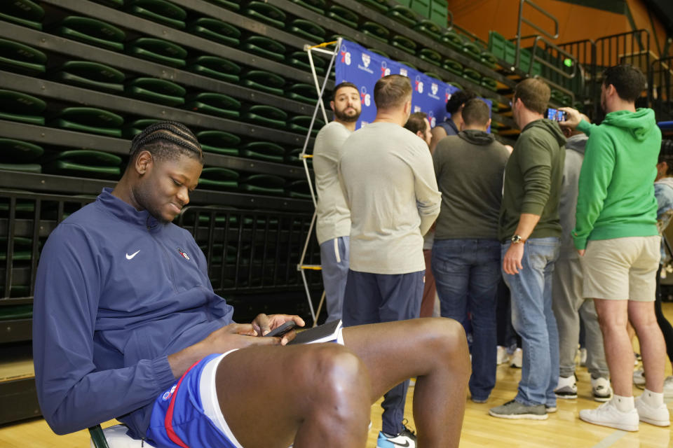 Philadelphia 76ers center Mo Bamba checks his mobile device while reporters crowd around center Joel Embiid during the NBA basketball team's practice Thursday, Oct. 5, 2023, in Fort Collins, Colo. (AP Photo/David Zalubowski)