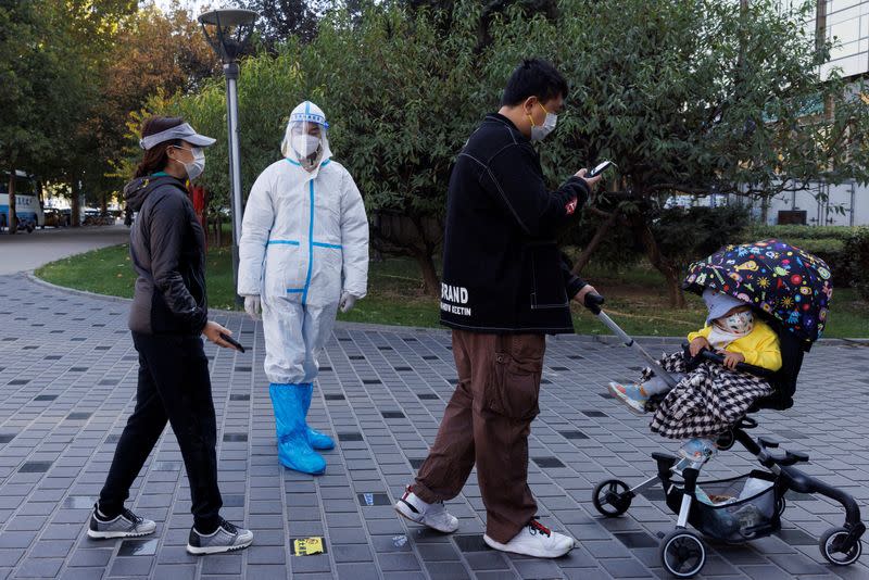 FILE PHOTO: A pandemic prevention worker wears a protective suit as people line up to get swab tests at a testing booth as outbreaks of coronavirus disease (COVID-19) continue in Beijing