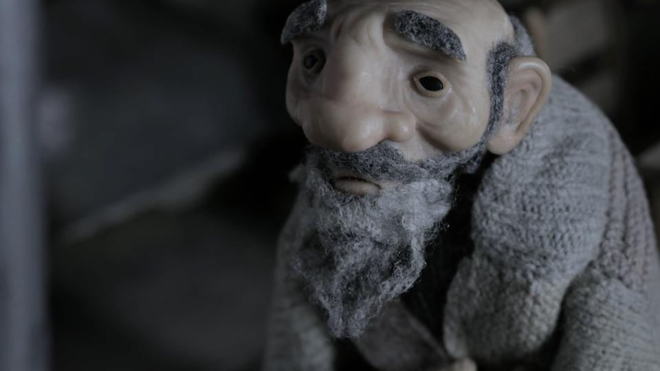 A clay figure of an old man with a beard wrapped in a blanket