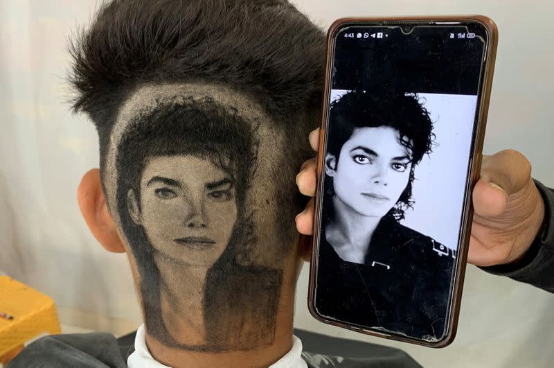 Gurwinder Singh Sidhu, a barber, displays a photo of Michael Jackson next to a customer after he made a hair tattoo of the pop star in the customer's hair inside his shop in Dabwali town, in the northern state of Punjab, India