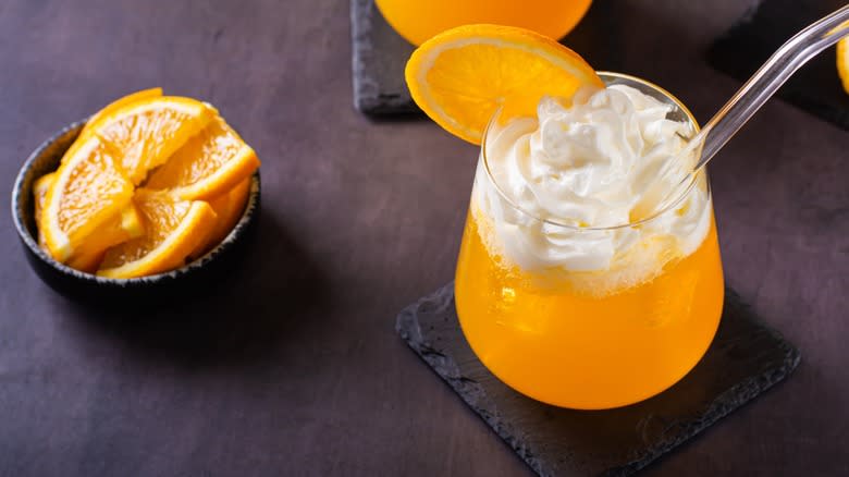 An orange soda with whipped cream and orange slices