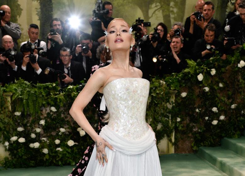 Ariana Grande poses in a white gown and tilts her chin up while walking a green carpet