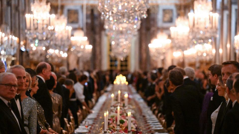 Candles and chandeliers illuminate the room as royals attend a state banquet at the Palace of Versailles