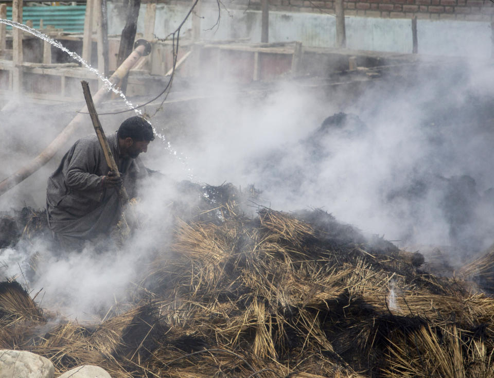 A Kashmiri man tries to douse the fire after fodder caught fire during a gun battle between government forces and suspected rebels in Bijbehara, some 28 miles (45 kilometers) south of Srinagar, Indian controlled Kashmir, Sunday, April 11, 2021. (AP Photo/Mukhtar Khan)