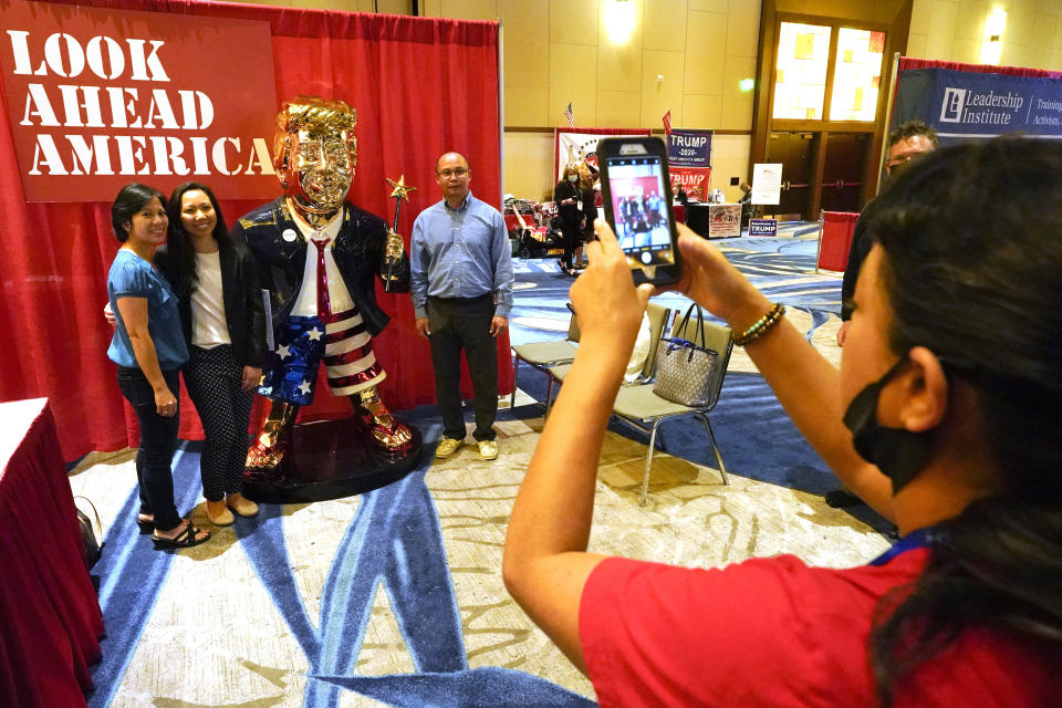 Conference attendees pose for a photo next to a statue of former president Donald Trump at the merchandise show at the Conservative Political Action Conference (CPAC) Saturday, Feb. 27, 2021, in Orlando, Fla. (AP Photo/John Raoux)