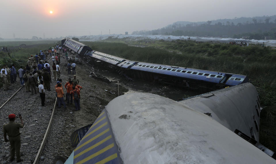 An Assam police officer, left, takes a photograph on his mobile of a train that derailed near Jagiroad Railway Station, about 90 kilometers (56 miles) east of Gauhati, India, Wednesday, April 16 2014. According to a Northeast Frontier Railway officer, dozens of people were injured when the train jumped the tracks and derailed early Wednesday. (AP Photo/Anupam Nath)