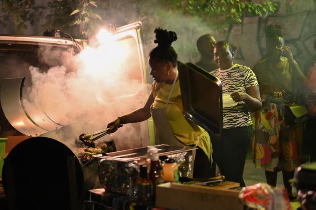 A woman grills jerk chicken on All Saints Road as the Mangrove Steelband rehearses. (Photo: Clara Watt for HuffPost)