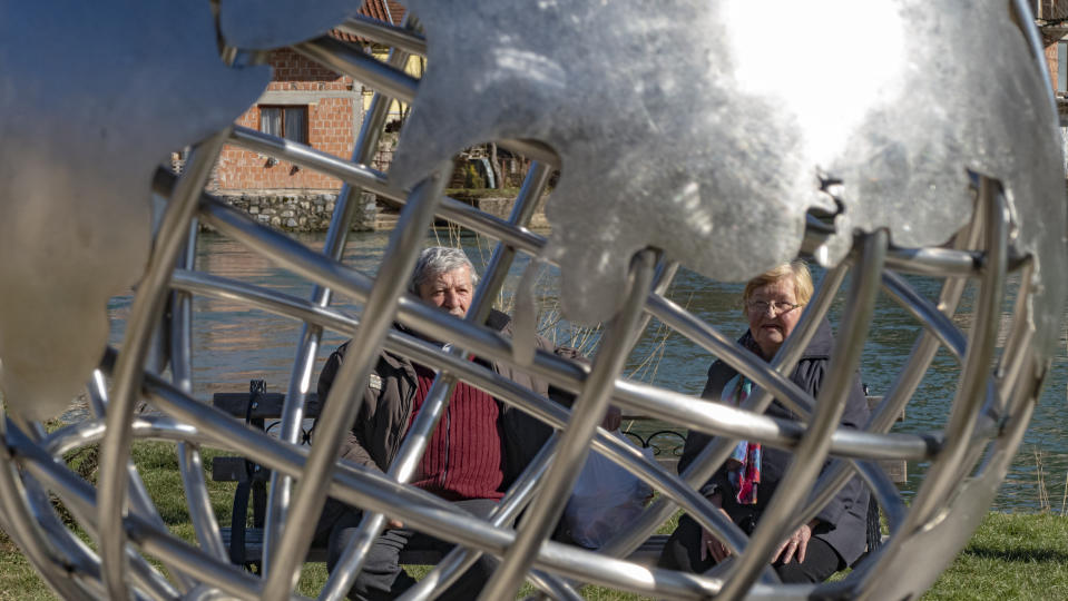 Residents are seen through a metal representation of planet Earth in Jezero, Bosnia, Tuesday, Feb. 16, 2021. Bosnian villagers are setting up a video screen in the yard of the village’s sole school so people can gather to watch NASA’s Mars rover land Thursday in a crater of the Red Planet named after their small village. It will be a historic day for the 1,000 villagers, who hope that the landing of the Perseverance rover in a crater on Mars will also bring them some earthly rewards. (AP Photo/Almir Alic)