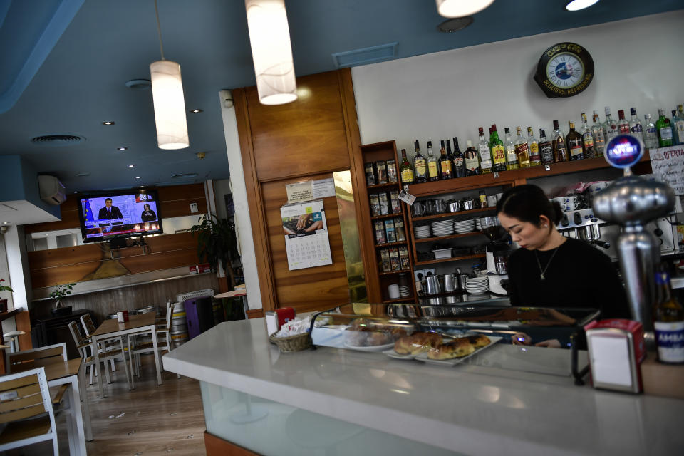 A Chinese woman manages a bar while Spanish Prime Minister Pedro Sanchez appears on TV, left, announcing new measures to fight against social and economic crisis caused by the COVID-19 coronavirus, in Pamplona, northern Spain, Thursday, March 12, 2020. For most people, the new coronavirus causes only mild or moderate symptoms, such as fever and cough. For some, especially older adults and people with existing health problems, it can cause more severe illness, including pneumonia. (AP Photo/Alvaro Barrientos)