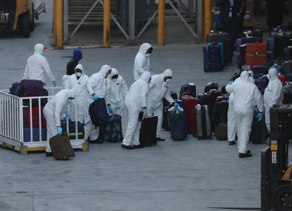 Workers dressed in hazmat suits take the luggage off the Zaandam cruise ship.