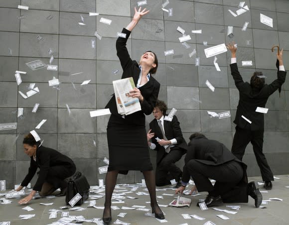 Picture of five business people on the sidewalk snatching money cash falling from the sky.