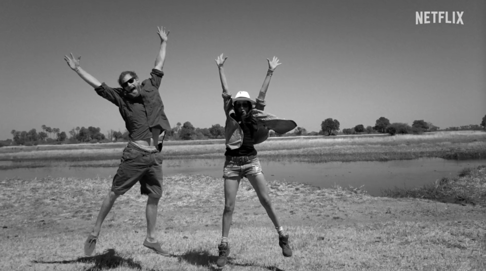 Harry and Meghan jump in the air in a field.