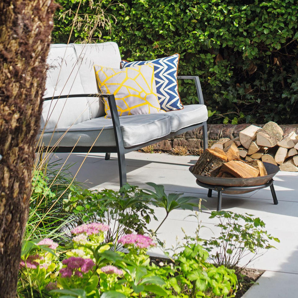 Outdoor sofa with colourful cushions on a stone path with a firepit