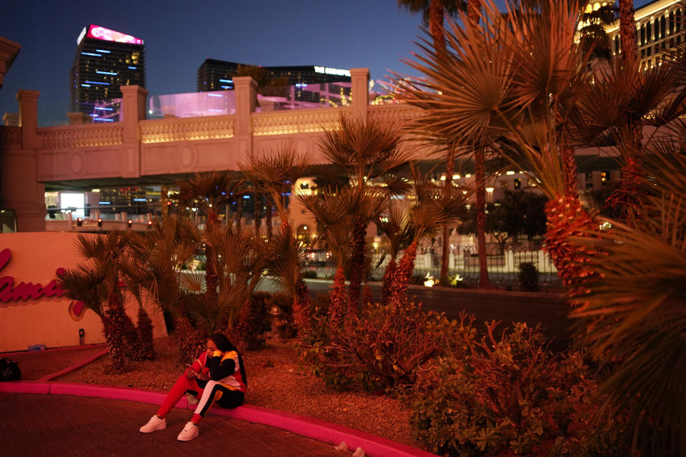 A woman sits on a curb along the Strip in Las Vegas, Feb. 10, 2021. Visitor numbers in Las Vegas were down by more than half in 2020 compared to 2019, according to data compiled by tourism, airport and gambling regulators. (AP Photo/John Locher)