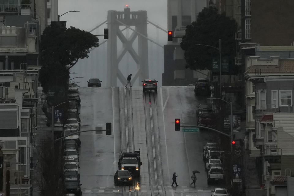 Pedestrians cross California Street in San Francisco, Friday, Feb. 24, 2023. California and other parts of the West are facing heavy snow and rain from the latest winter storm to pound the United States. The National Weather Service has issued blizzard warnings for the Sierra Nevada and Southern California mountains. (AP Photo/Jeff Chiu)