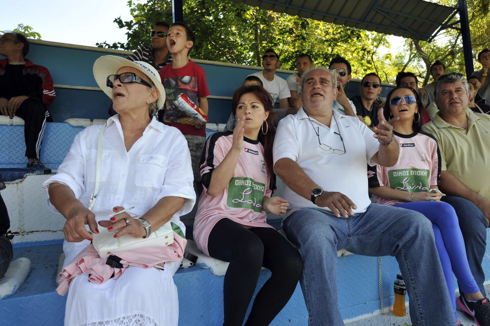 In this photo taken Sunday, Oct. 7, 2012, brothel owner Soula Alevridou, left, the benefactor of the Voukefalas amateur soccer team, reacts during a local championship match in the city of Larissa, central Greece. A cash-strapped Greek soccer team has found a new way to pay the bills, with help from the world’s oldest profession. Players are wearing bright pink practice jerseys emblazoned with the logos of the Villa Erotica and Soula’s House of History, a pair of pastel-colored bordellos recruited to sponsor the team after drastic government spending cuts left the country's sports organizations facing ruin. One team took on a deal with a local funeral home and others have wooed kebab shops, a jam factory, and producers of Greece’s trademark feta cheese. But the small amateur Voukefalas club which includes students, a bartender, waiters and pizza delivery drivers is getting the most attention for its flamboyant sponsors. Logo on T-shirts translates to 'Soula's House of History'. (AP Photo/Nikolas Giakoumidis)