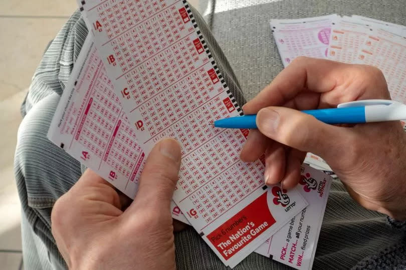 Picture of someone's hands filling out a Lottery Ticker with a pen.