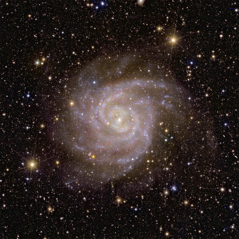 A spiral galaxy is seen in the center of the image.  In the background there is a wealth of stars and galaxies in space.