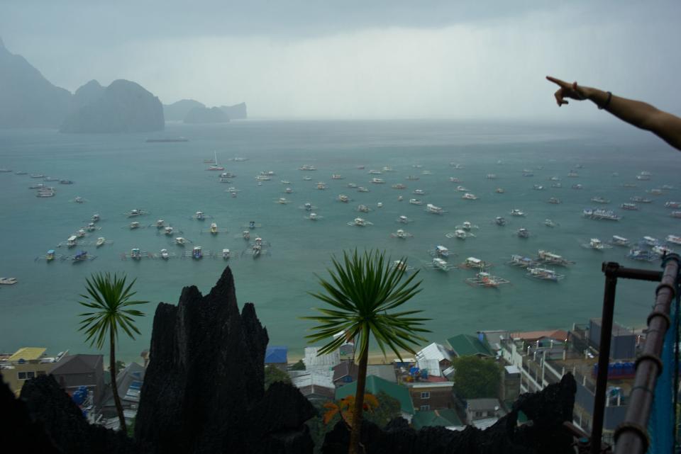 Boats are scattered across the water as a person points to something to in the distance in El Nido, Philippines.