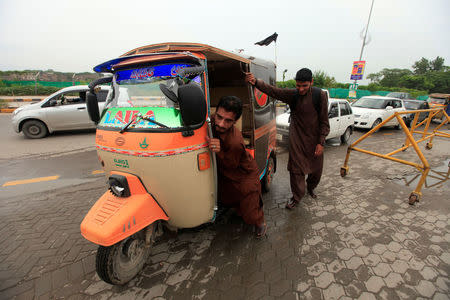 A driver who has run out of fuel pushes his rickshaw into a petrol station in Rawalpindi, Pakistan July 26, 2017. REUTERS/Faisal Mahmood