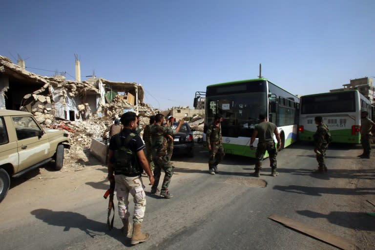 Syrian troops stand guard as a bus carrying people drives by, as part of an evacuation from the town of Daraya outside the capital Damascus on August 26, 2016